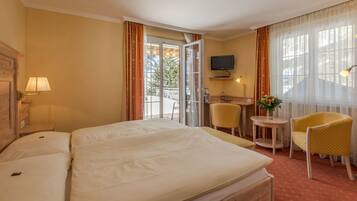 A hotel room with a large bed, a desk with a chair, a television, and a view of the outdoors.