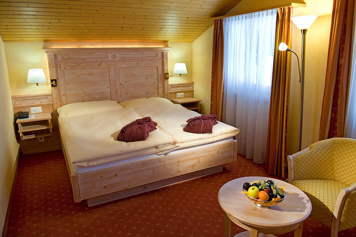 Habitación de hotel con una cama grande, dos lámparas de noche, una mesita con fruta y una silla.