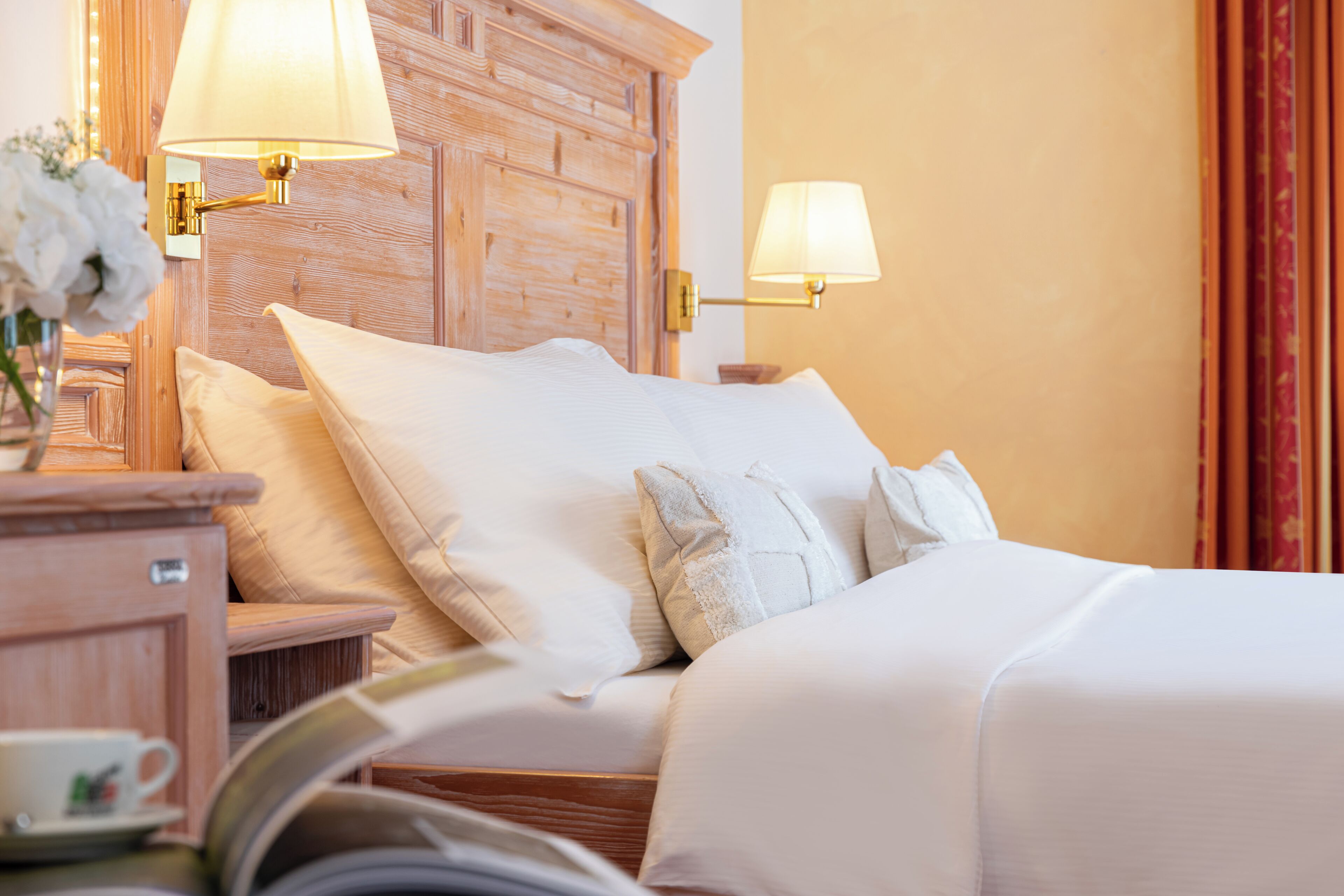 Un lit bien fait, avec du linge de lit blanc et des oreillers, une tête de lit en bois et deux lampes fixées au mur.
