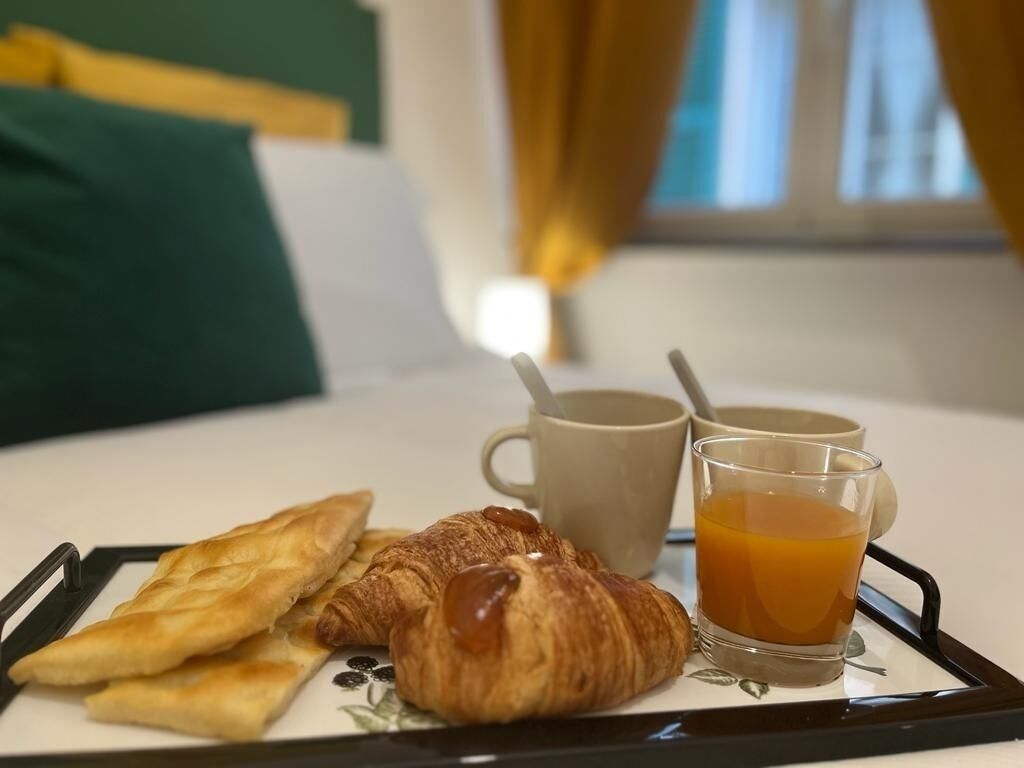 Een ontbijttafel met gebak en een glas sinaasappelsap, in een kamer met een bed en gordijnen op de achtergrond.
