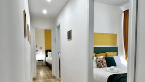 Ein Flur, der zu einem Schlafzimmer mit Bett, Kopfteil und einem mit Vorhängen versehenen Fenster führt.