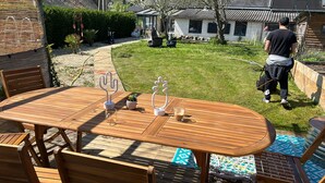 Eine Holzterrasse mit Tisch und Stühlen, einem dekorativen Metall-Pflanzgefäß und einem Glas Eistee.
