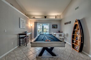 Relax in a spacious room with a pool table, bar, and bookshelf, featuring a large window and outdoor access.