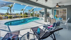 Un espace aménagé au bord de la piscine, avec des chaises longues, une table et un ventilateur de plafond.