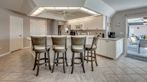 Une cuisine moderne dotée d’un îlot central, de tabourets de bar et d’un ventilateur de plafond.
