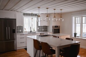 A modern kitchen with white cabinetry, a central island, hanging glass pendant lights, and a large window.