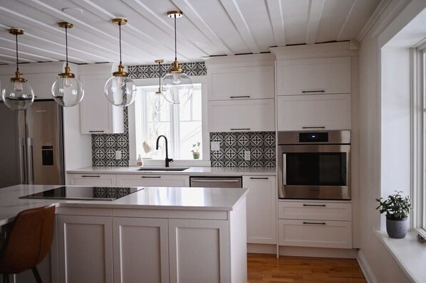 A modern kitchen with white cabinetry, a central island, pendant lights, and a large window.