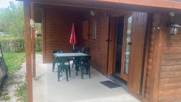 En træhytte med en overdækket terrasse, et bord med stole og en rød parasol.
