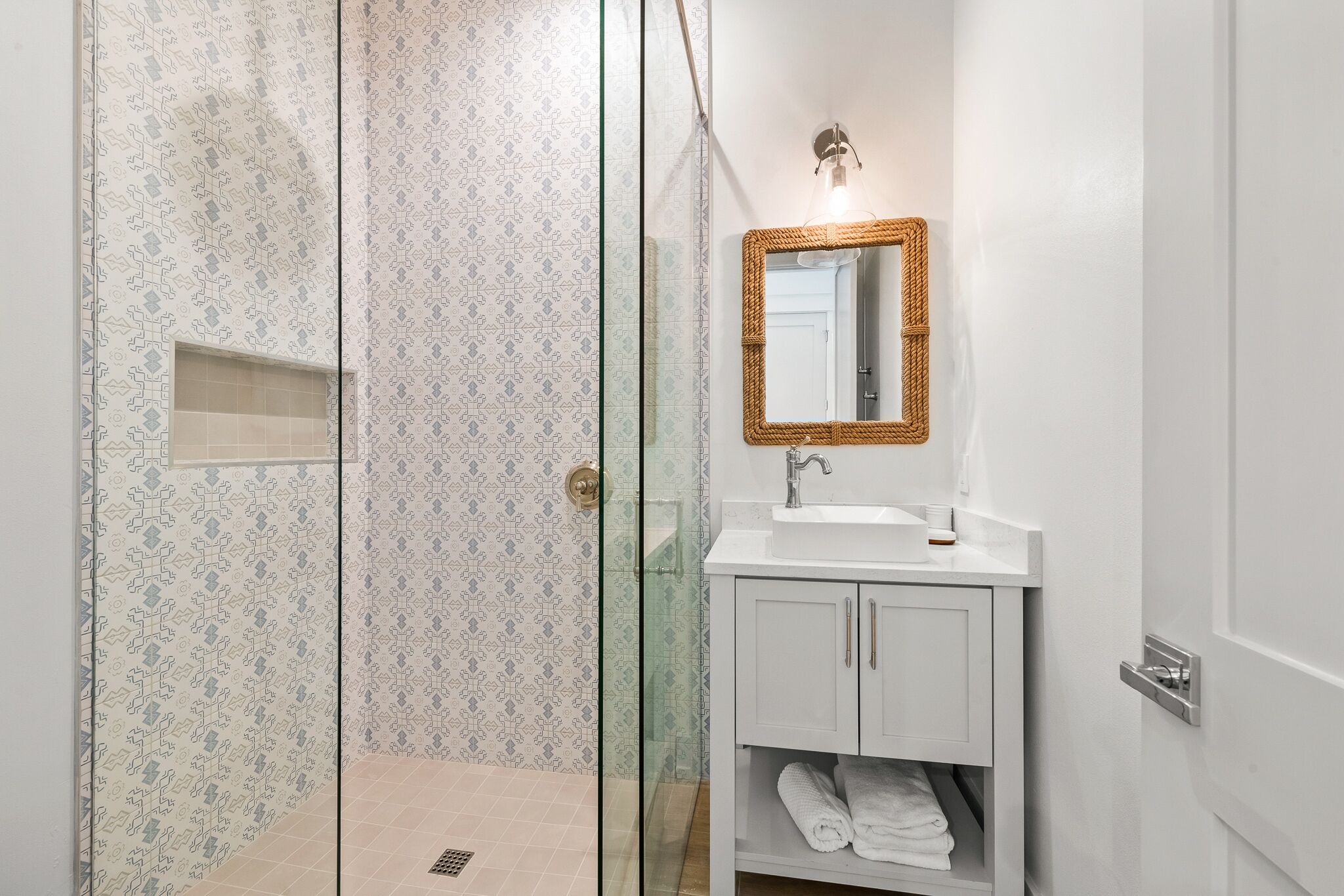 A bathroom with a glass shower enclosure, a white sink with a mirror, and a towel rack.