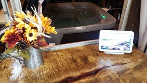 A wooden table with a metal bucket containing a floral arrangement, a hot tub, and a tablet displaying an image.