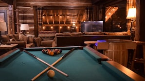 A pool table with balls, a sofa, and a television in a room with wooden walls and a window.