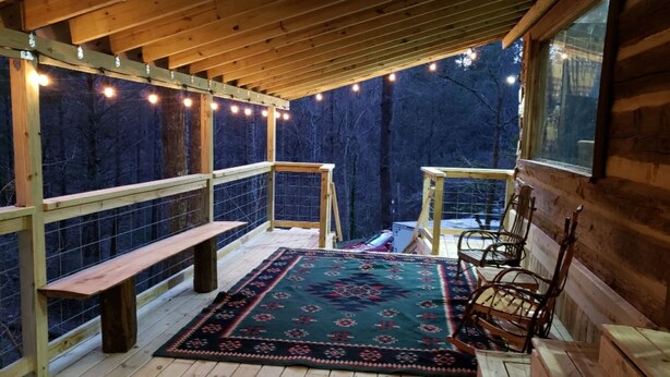 A wooden deck with a bench, chairs, and a rug.