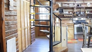 A rustic interior with a spiral staircase, wooden walls, and a kitchen area.