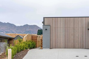 A modern building with a wooden facade, a concrete entrance, and a view of mountains in the background. - Northlake Alpine Retreat (Wanaka)