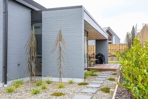 A modern house with a grey exterior, a wooden deck, and a gravel pathway leading to the entrance. - Northlake Alpine Retreat (Wanaka)