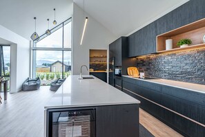 A modern kitchen with a large island, dark cabinetry, and a stone backsplash.