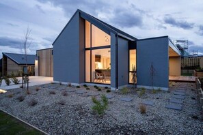 A modern house with a large open-plan interior, a visible kitchen area, and a gravel driveway.