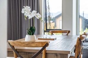 A wooden dining table with a white vase of white flowers, a book, and a woven placemat.