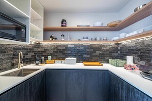 A modern kitchen with dark cabinetry, a built-in microwave, and a stone backsplash. - Northlake Alpine Retreat (Wanaka)