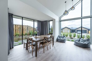 A spacious room with a large dining table and chairs, a seating area with bean bags, and large windows offering a view of the outside.