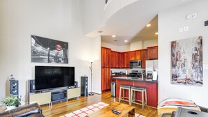 A modern living room with a flat-screen TV, leather sofas, a coffee table, and a kitchen in the background. - Dtwn Houston Home Near Stadiums: WFH Friendly! (Houston)