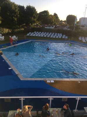 A swimming pool with people swimming and a lounge area with chairs.