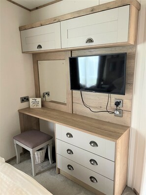 A compact room with a built-in TV, a small desk with drawers, and a bench.