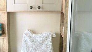 Ein Badezimmer mit Holzausbau über einem weißen Heizkörper, ein Handtuch, das am Heizkörper hängt, und einer Duschkabine aus Glas.