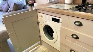 Eine kleine Küche mit Einbauwaschmaschine, einer Holzarbeitsplatte und einem beige gefärbten Schrank mit Schubladen.