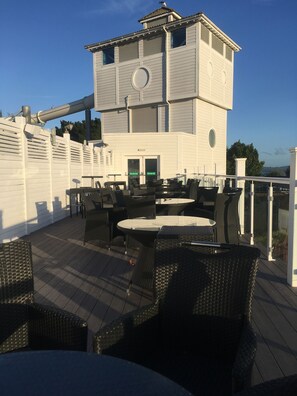 A rooftop patio with wicker furniture and a white building with a circular window. - Sunflower -  premier dog-friendly caravan on Rockley Park  (Poole)