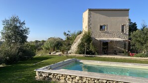 A stone building with a pool, surrounded by greenery and trees.