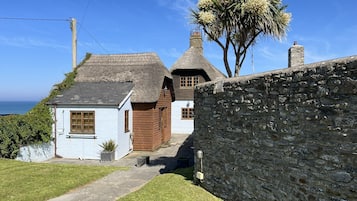 A traditional stone house with a thatched roof, a wooden door, and a white exterior wall.