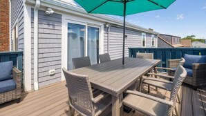 Eine Terrasse mit Tisch und Stühlen, einem grünen Sonnenschirm und einem Haus mit hellgrauem Putz.
