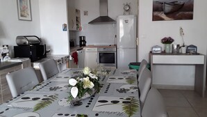 Een kleine keuken met een koelkast, oven en koffiezetapparaat. Een eettafel met stoelen is gedekt, met een bloemige decoratie in het midden.