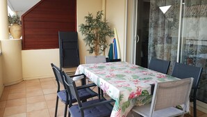 Een terras met een tafel, stoelen, een schuifpui, een bloempot en een houten constructie.