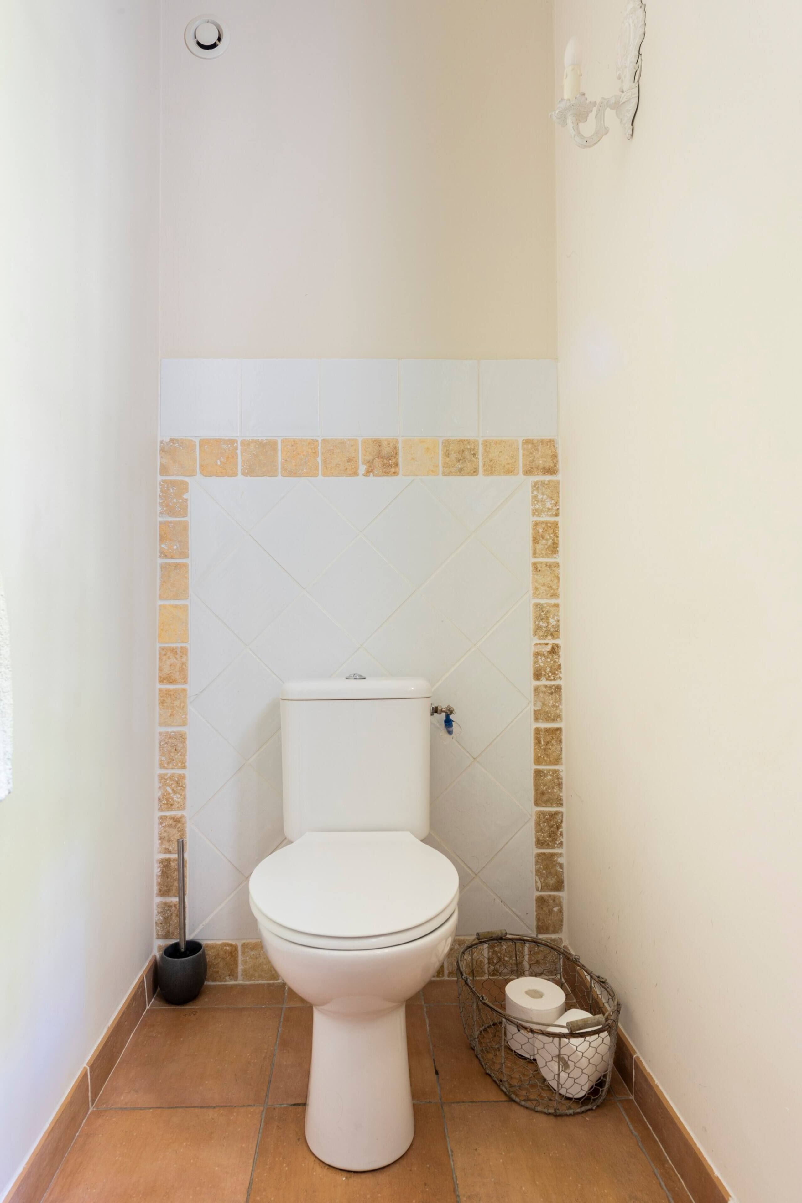 A small bathroom with a white toilet, a tiled floor, and a wall-mounted light fixture.