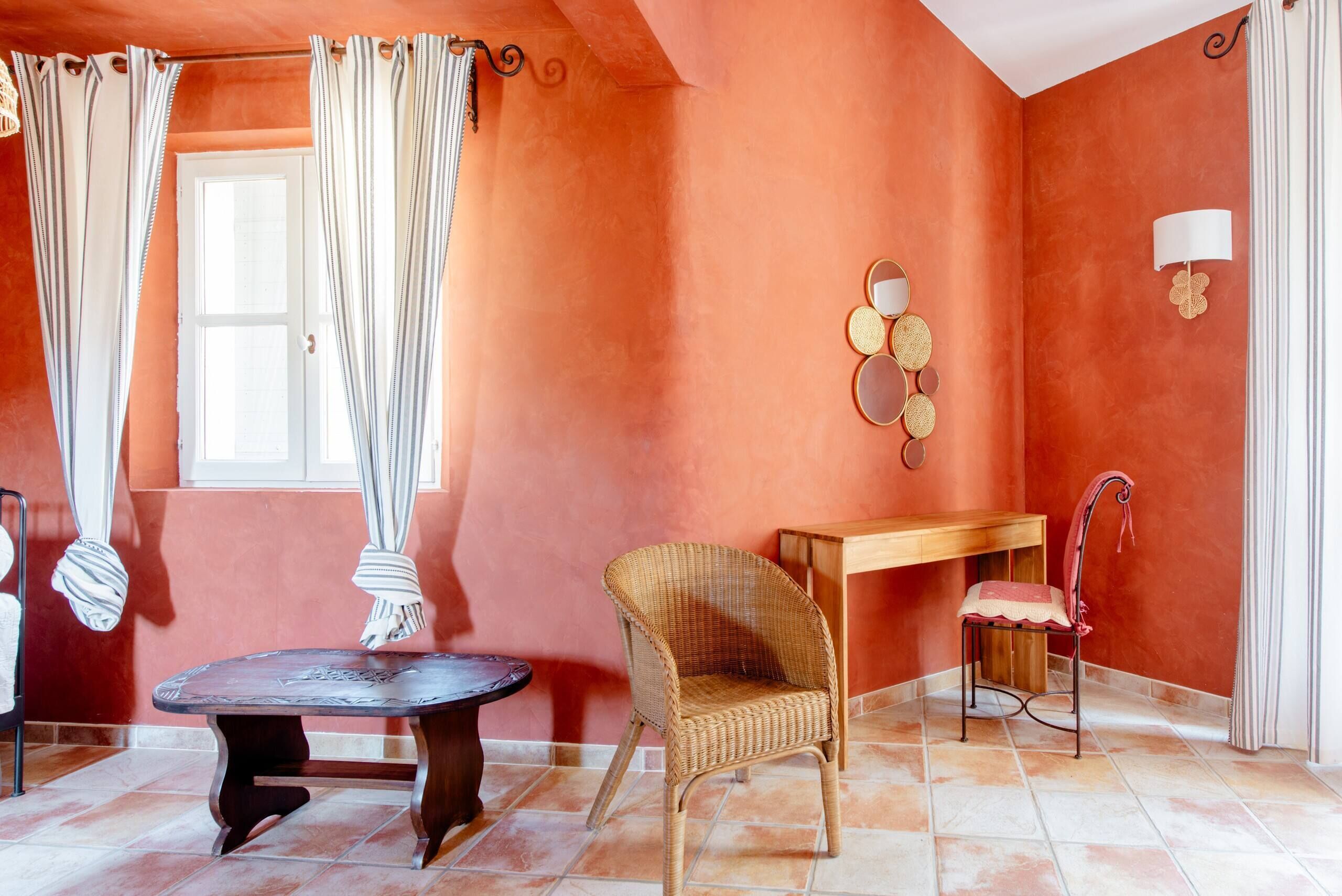 A room with a wicker chair, a wooden table, and a small wooden bench.
