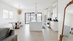 Una cucina moderna con mobili bianchi, un'isola in marmo e una zona pranzo con tavolo e sedie.