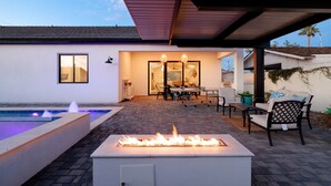 Una moderna terrazza esterna con un elemento decorativo a fuoco, una piscina e un'area pranzo con sedie e tavolo.