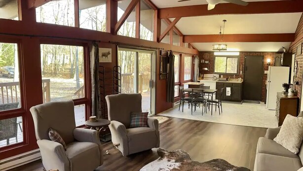 A spacious living room with a large window, a ceiling fan, and a rustic leather rug. - City Escape: Cozy 2 bedroom Chalet in Jim Thorpe (Jim Thorpe)