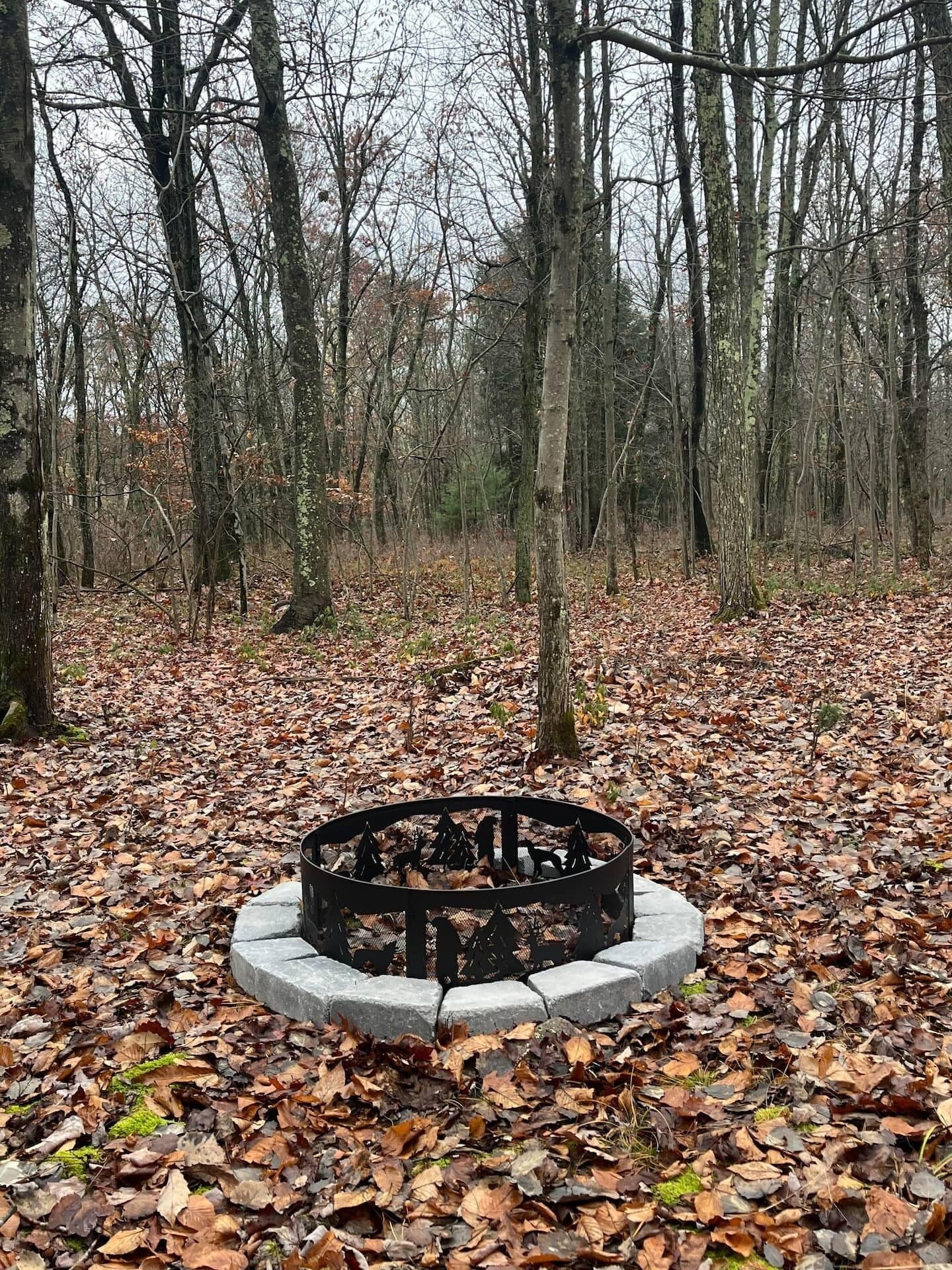 Un banco de piedra circular rodeado por una valla metálica en un área boscosa con hojas caídas.