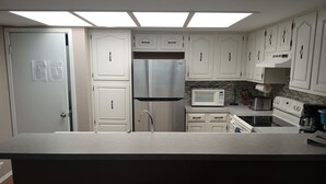 A kitchen with white cabinets, a stainless steel refrigerator, a microwave, a stove, and a sink. - SUNNY SIDE UNIT 210  (South Padre Island)