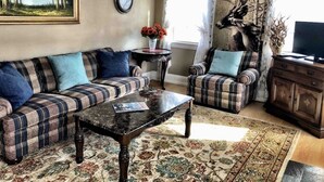 Un salon avec un canapé, un fauteuil, une table basse et un tableau accroché au mur.