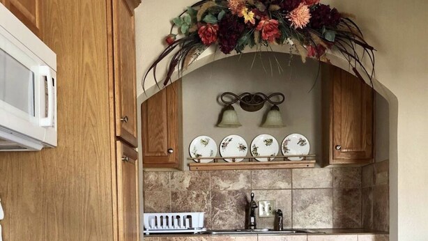 Une cuisine avec des meubles en bois, un four blanc, un évier et un arrangement floral décoratif placé au-dessus de l’évier.