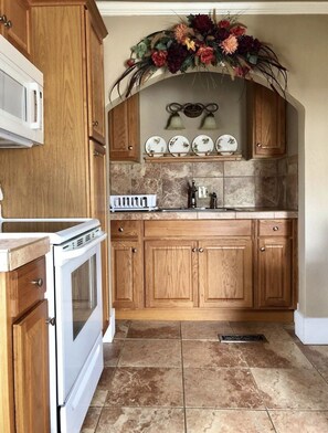 A kitchen with wooden cabinets, a white stove, a sink, and a decorative floral arrangement above the sink.