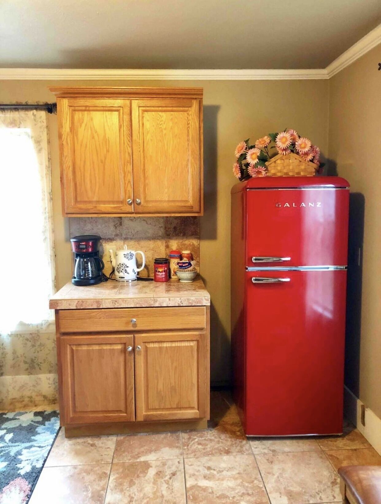 A compact kitchen with wooden cabinets, a red Galanz refrigerator, and a countertop with a coffee maker, kettle, and jars.