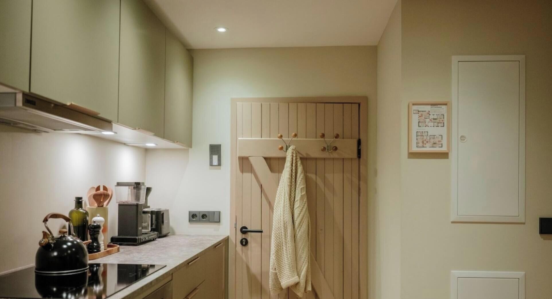 Een kleine keuken met een houten deur, een koffiezetapparaat en een waterkoker op het aanrecht.