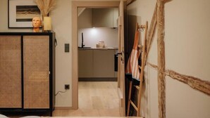 Una stanza con un letto, un armadio, una scrivania con una lampada e un angolo cottura visibile attraverso una porta aperta.