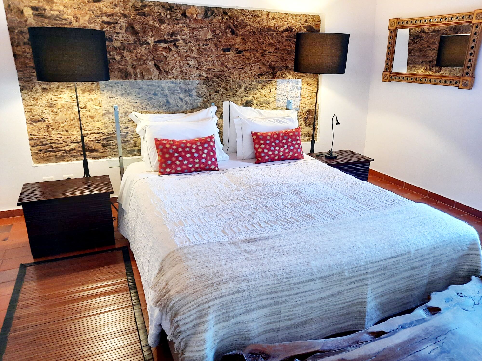 Un dormitorio con una cama grande, dos mesitas de noche, una pared de piedra y dos lámparas de pared.