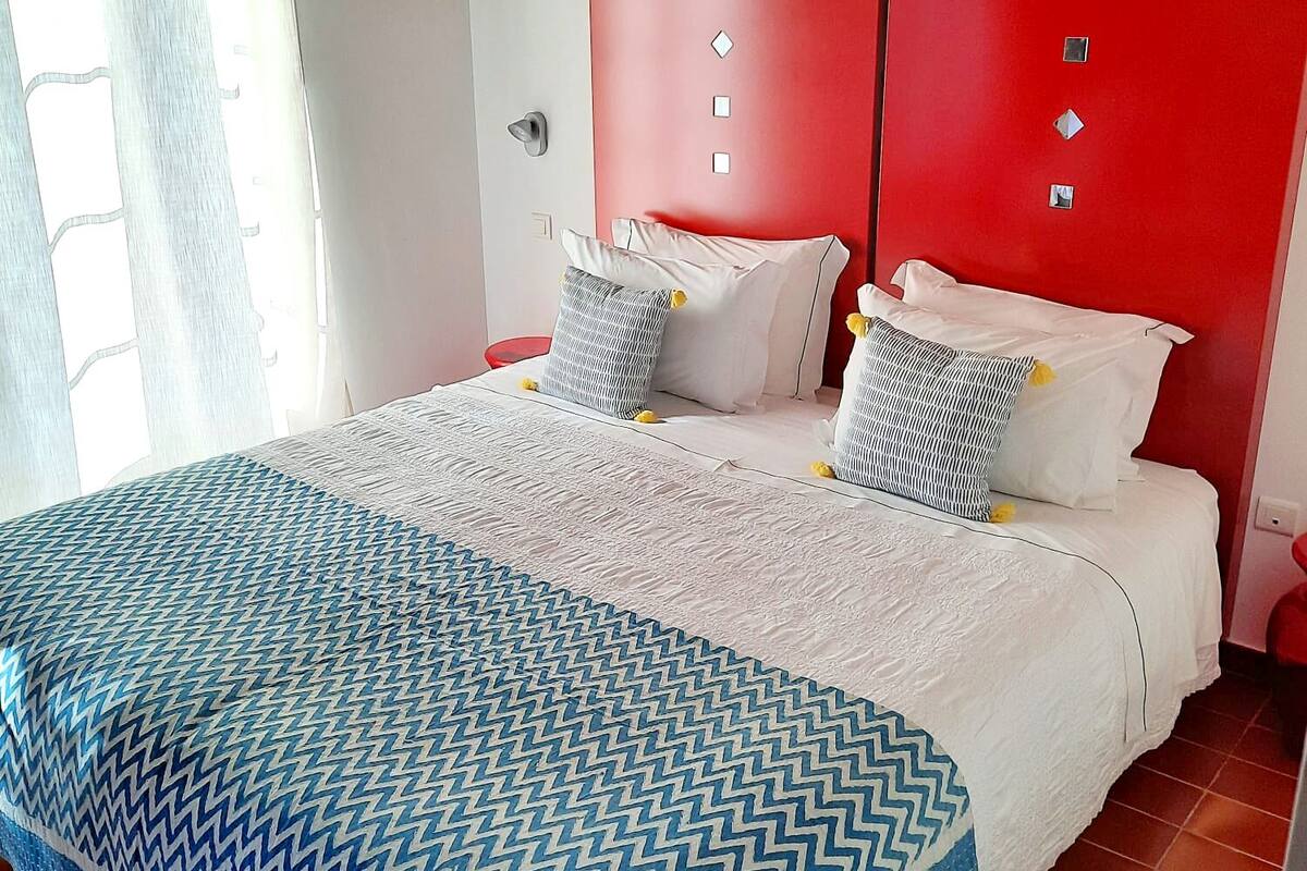 Ein Schlafzimmer mit einem Bett, einem roten Kopfteil und einem Fenster mit Vorhängen.